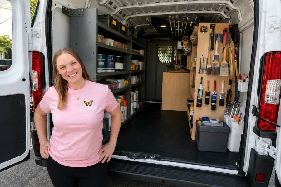 Ashley Rios smiling at the open back doors of the Monarch Painting van, shelves of paint and brushes behind her