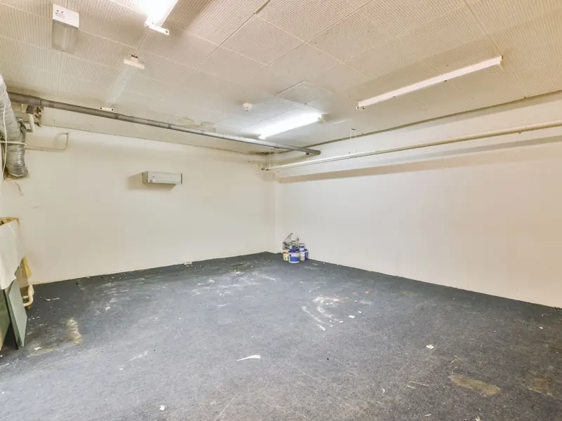 Basement with ceiling tiles, exposed pipes, and walls all painted white