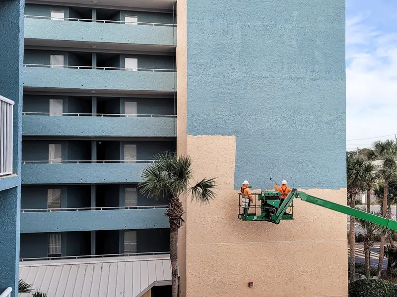 Painters on a lift coating a commercial building exterior wall