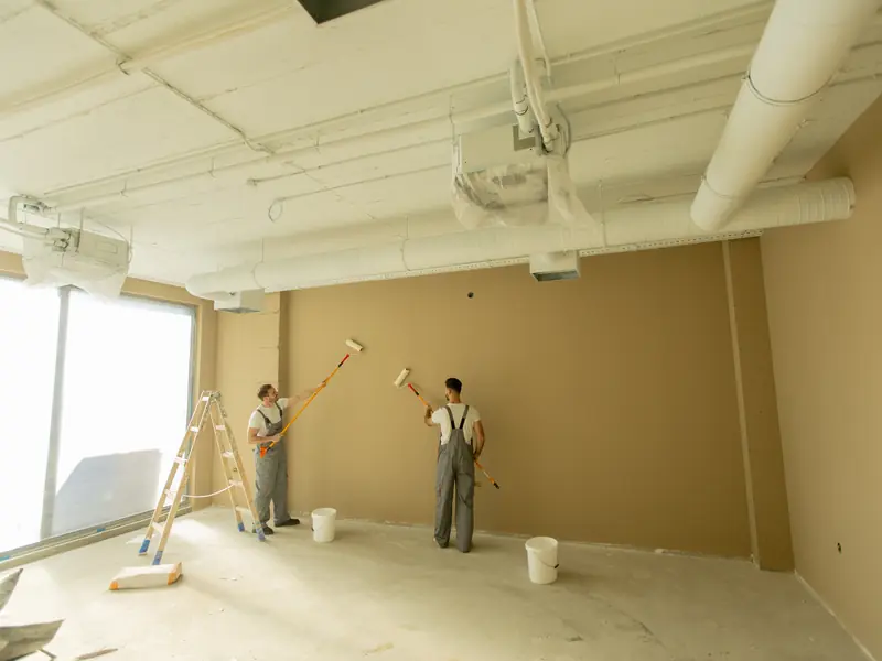 Two painters rolling a commercial interior wall in a bright space