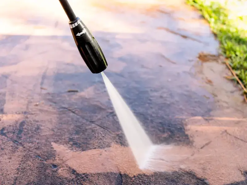 Close up of a pressure washer nozzle stripping dirt from a concrete driveway