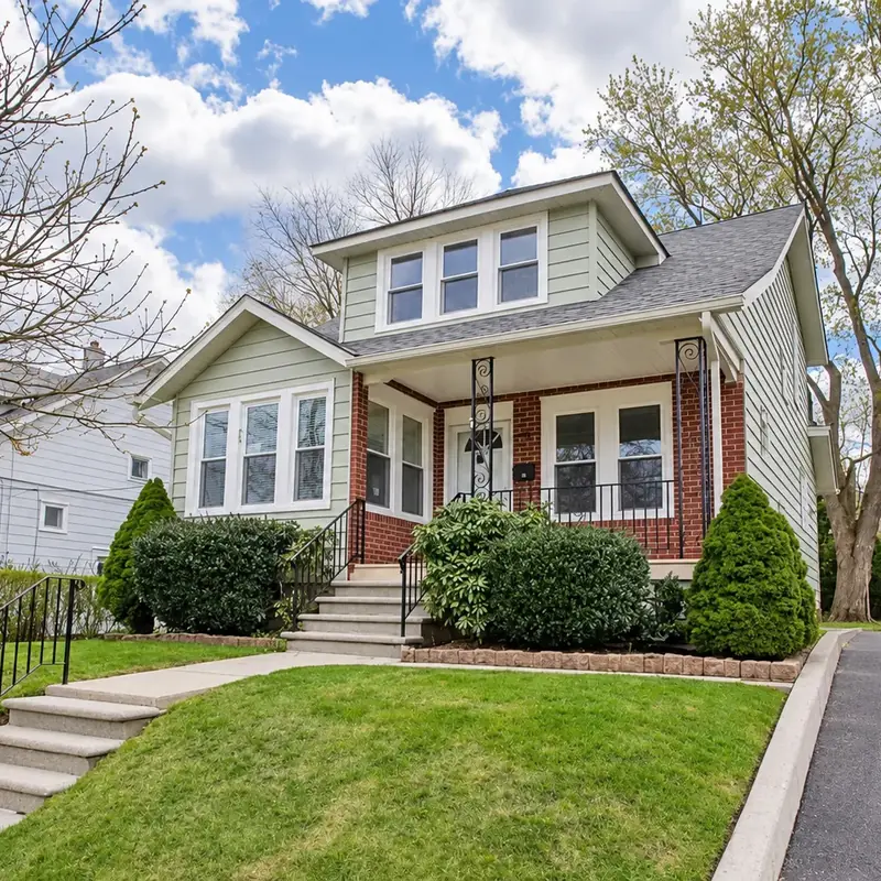 Sage green bungalow with white trim, brick porch, and black iron railings after exterior painting