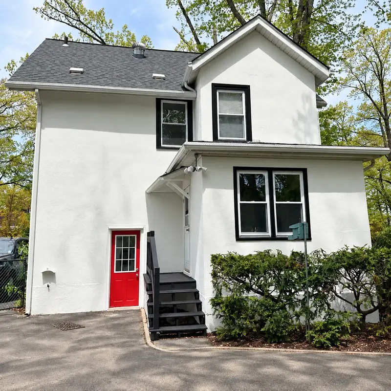White stucco home with black window trim and a red side door after exterior painting