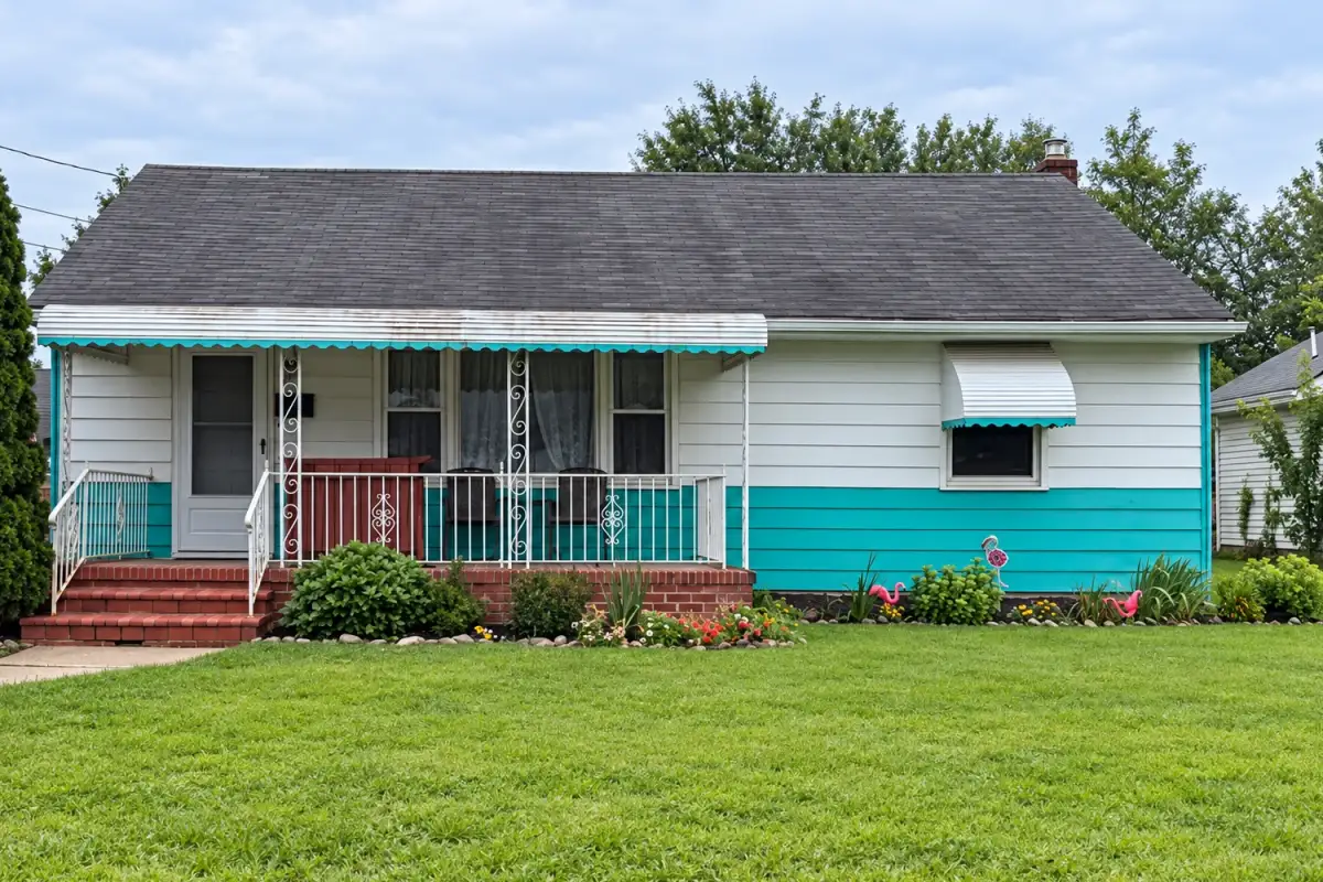 Single-story home with faded white and teal siding and a rusted awning before exterior painting