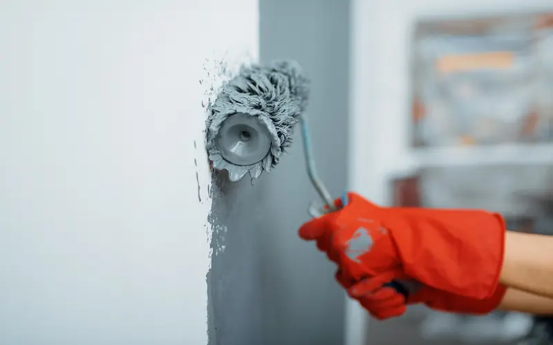 Painter rolling a bedroom wall with a cost estimate clipboard in the foreground