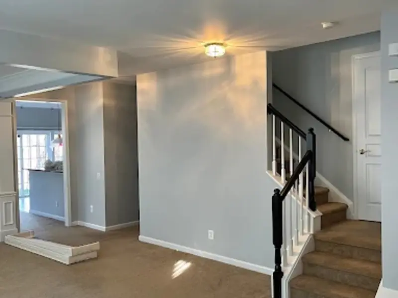Open living room and foyer painted soft gray with white trim and a black-railed staircase