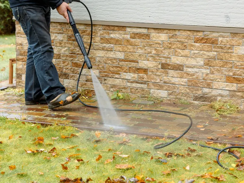 Pressure washing brick pavers along a stone foundation, weeds and grime rinsing away