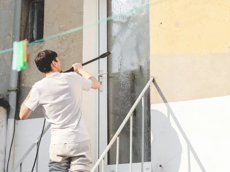 Technician power washing an exterior door and stucco wall from the front steps